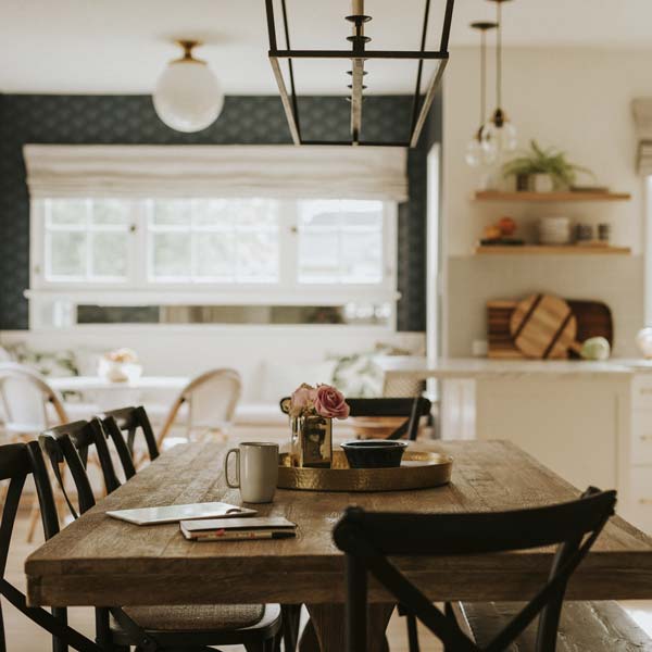 Close up of a oak dining table with cup, phone and newspaper on - with a out of focus kitchen in the background.